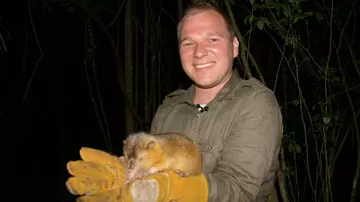 Photograph at night of Sam wearing thick gloves and holding a Hispaniolan solenodon in Dominican Republic