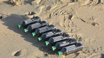 seven GPS tracked bottles lined up on beach
