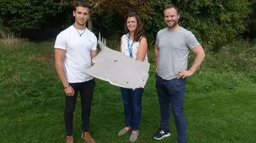Three people pose outside with an angelshark model