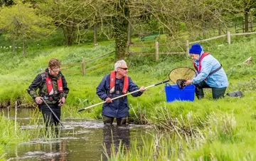 3 people catching trout on a river bank with a new