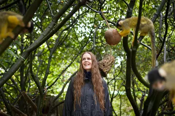 Linder Sterling standing in amongst trees in London Zoo's squirrel monkey habitat, with monkeys around her