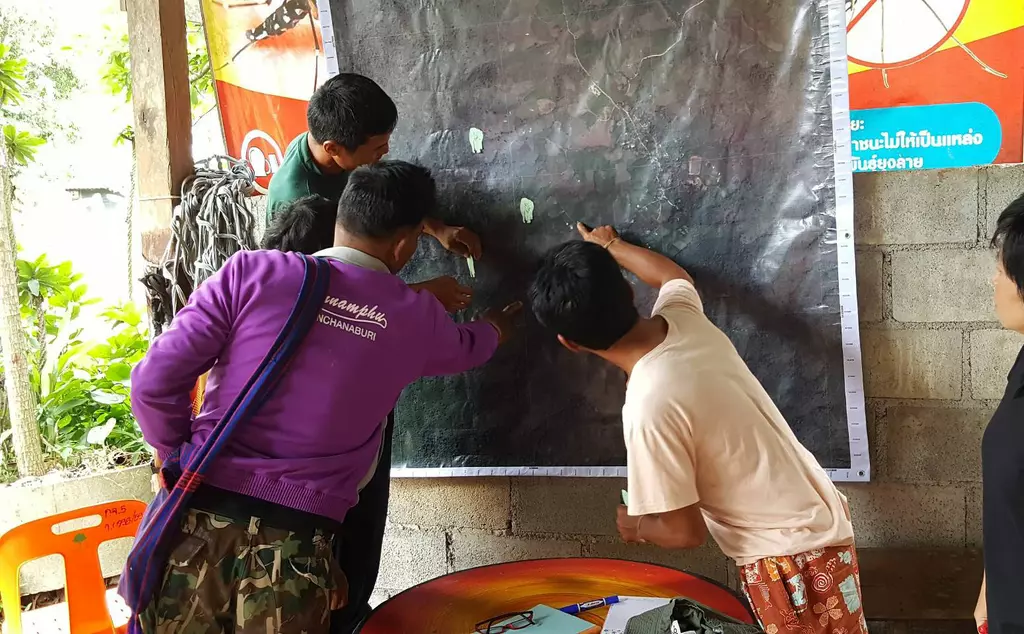 Three people pointing on a map tracing elephant entry and exit routes