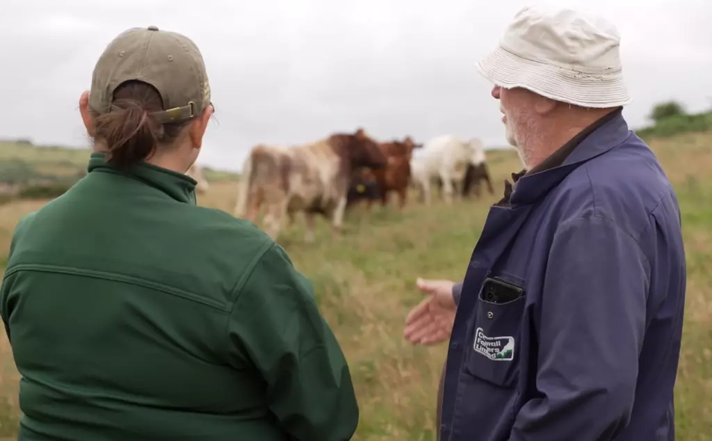 Conservationist and farmer stand talking, with cows in background