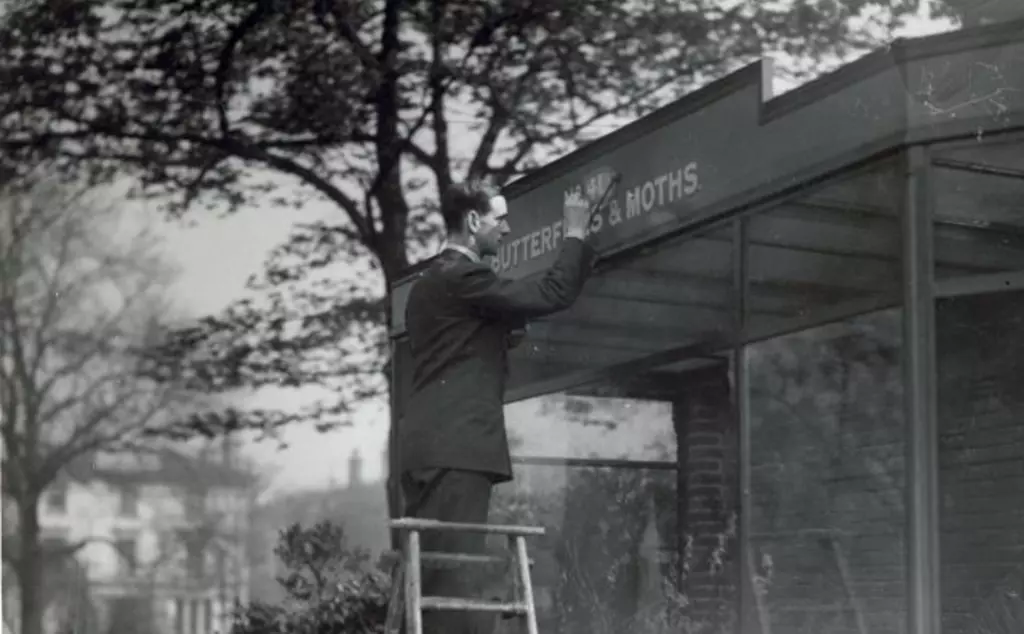 A black and white photo of a man standing on a ladder sign writing