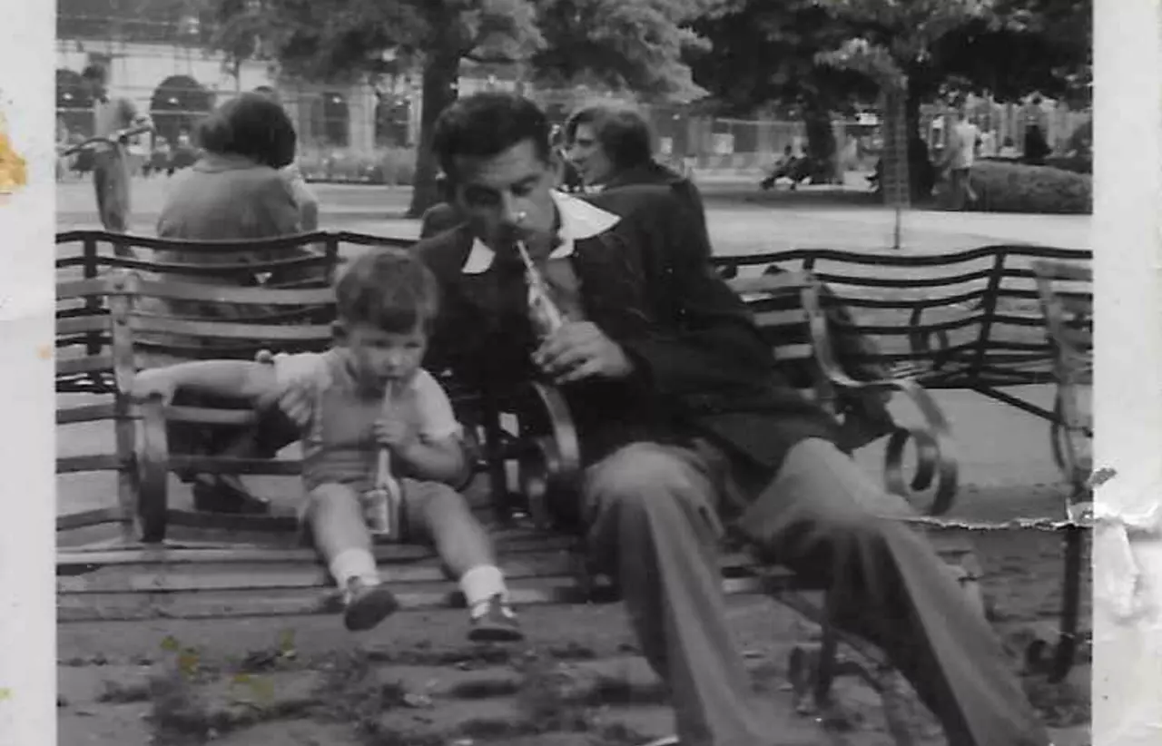 A black and white photograph of a child sitting on a bench with an adult