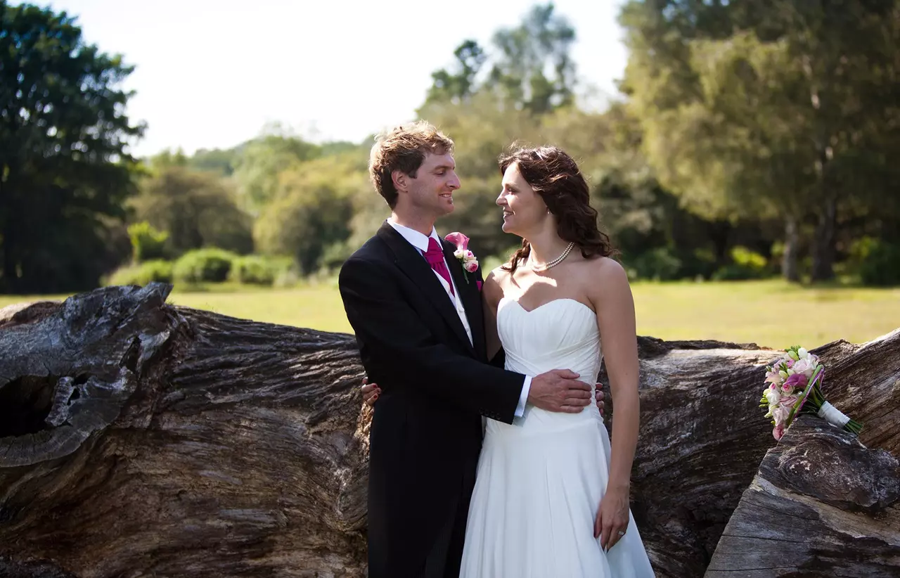 A husband and wife on their wedding day standing next to a log with greenery in the background