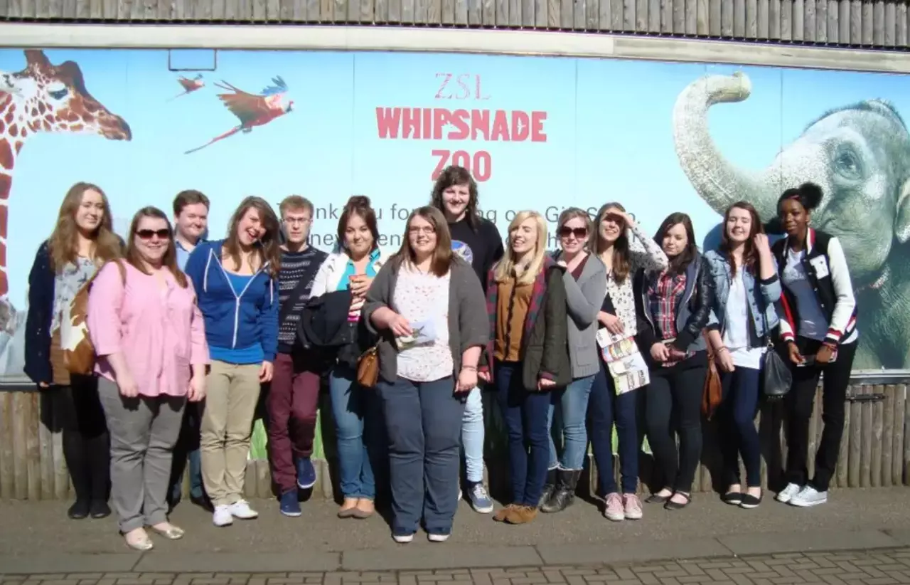 A group of visitors standing in front of a large ZSL Whipsnade Zoo poster