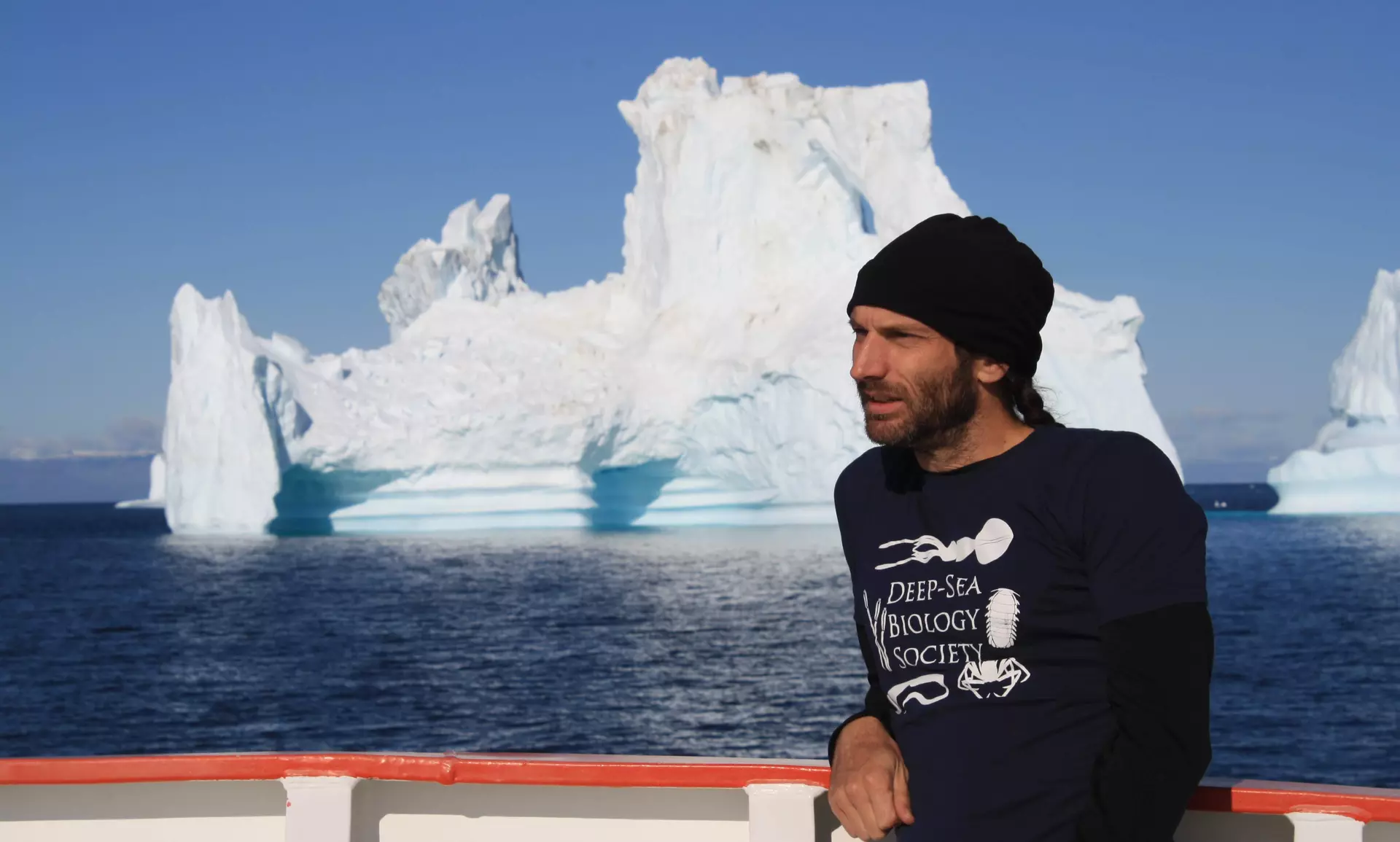 A man on a boat with an iceberg behind him