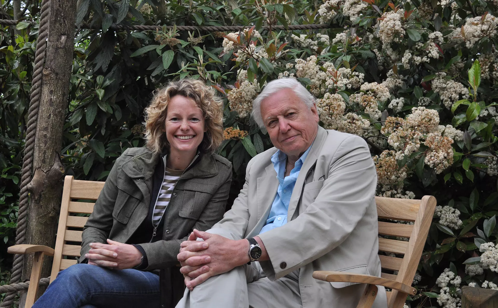 Kate Humble and David Attenborough sitting on a bench with greenery in the background