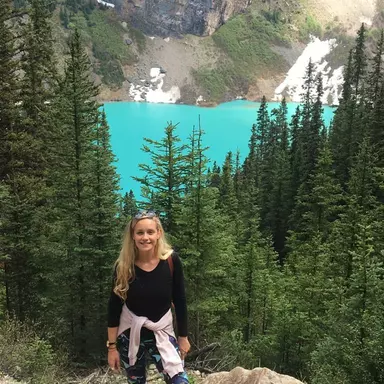 Shauna standing in front of a tree line with Lake Louise in the background