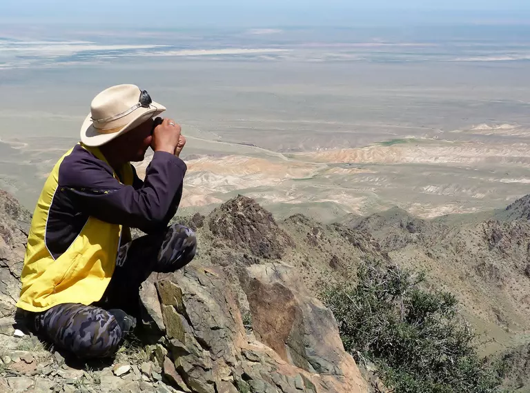 ZSL conservationist looking out at steppe habitat with binoculars on top of mountain in Mongolia,