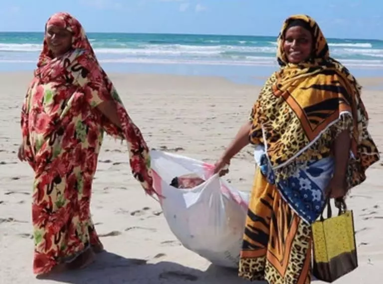 Two ladies collecting litter on a beach in Kenya