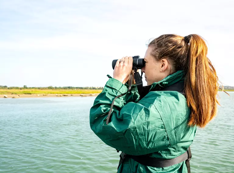 Woman looking through binocular at a river bank 