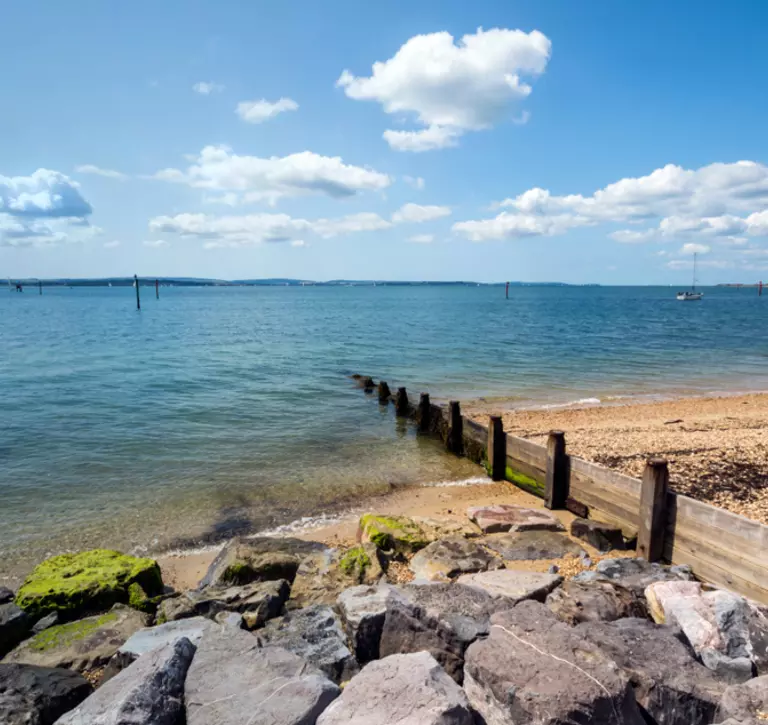 Lepe Bay beach, with rocks and sand in the foreground overlooking the sea