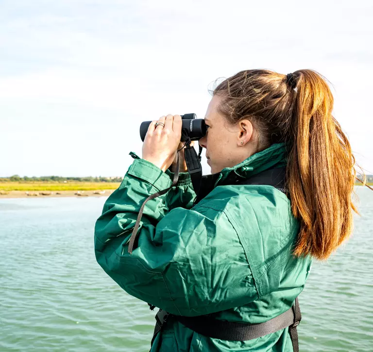 Woman looking through binocular at a river bank 