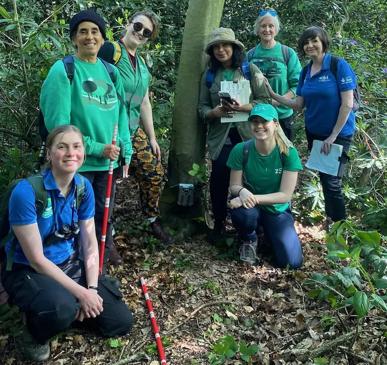 Group of volunteers smiling in front of a camera trap attached to a tree