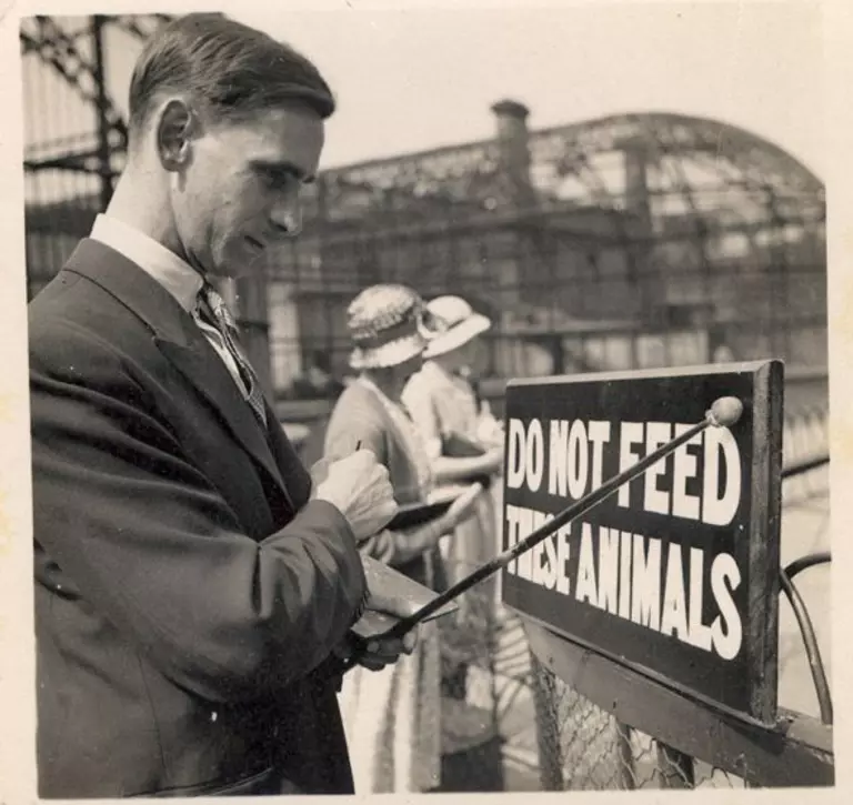 A black and white photo of a man sign writing. The sign says Do not feed the animals