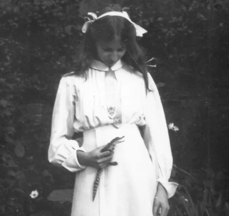 A black and white photograph of a young Joan Procter holding a crocodile