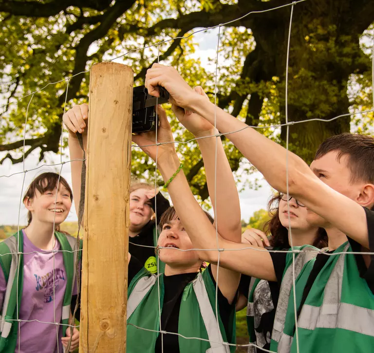 Students placing a camera trap on a fence